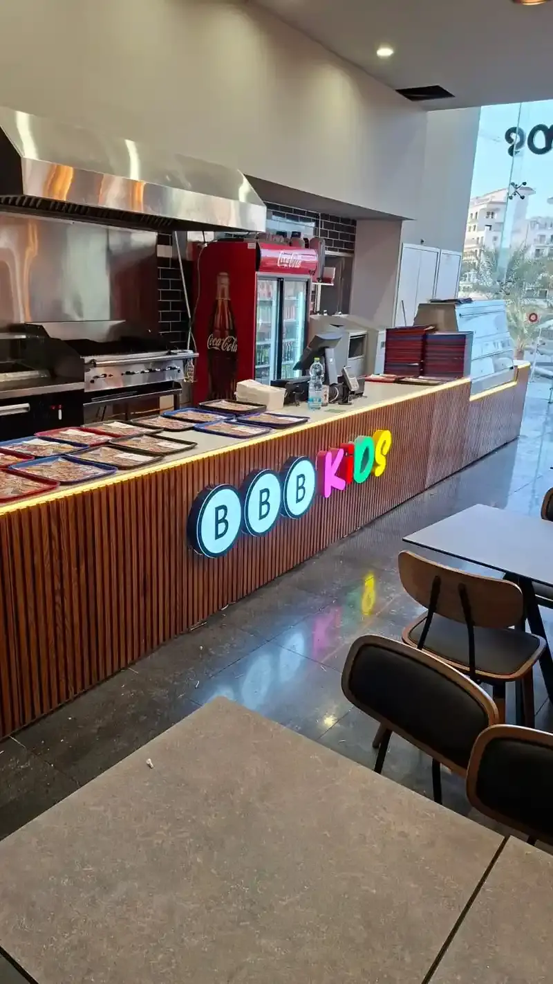 Illuminated interior letters mounted on a wooden slat service counter inside a restaurant, kitchen line behind