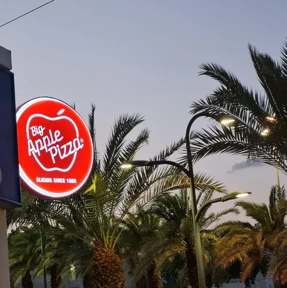 Round double-sided illuminated flag sign in red plexiglass, projecting on a bracket above a pizzeria entrance — SignWorks