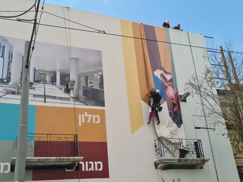 Installers on ropes fitting a building-sized printed sign